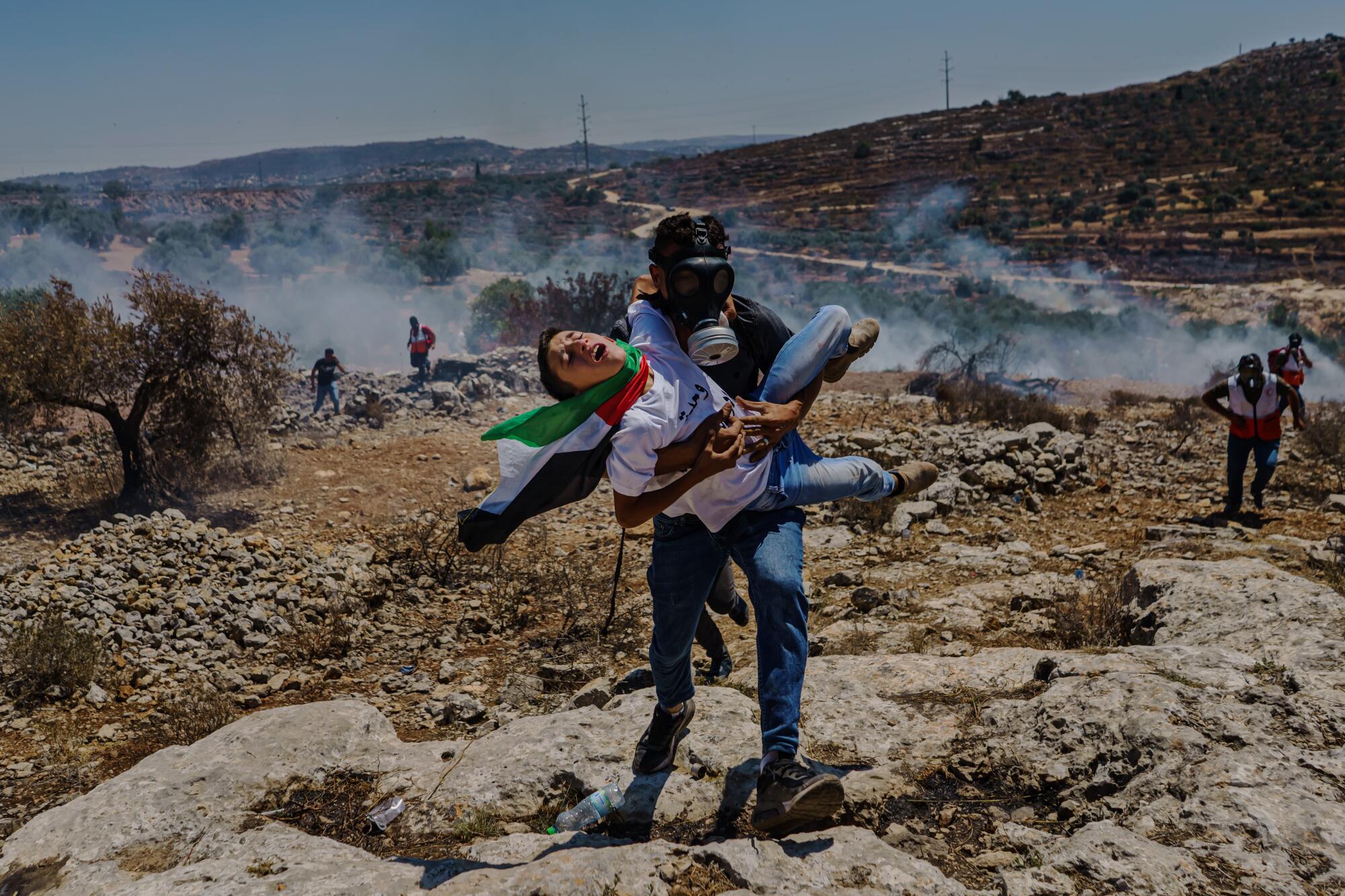 A young person is carried away from a protest by another person in a gas mask