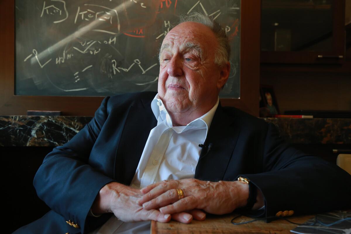 A man sits at a table in front of a blackboard with scientific computations