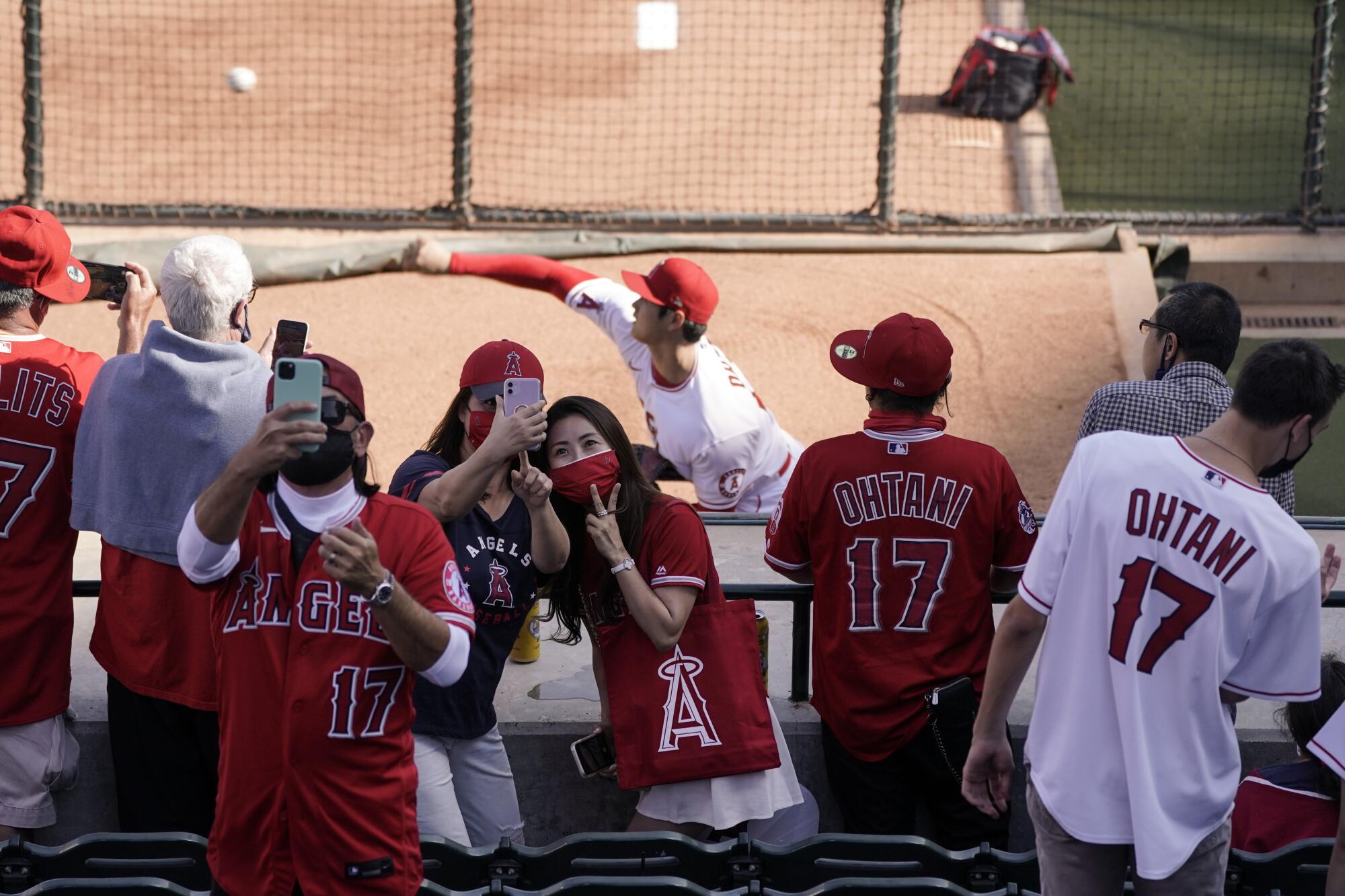 Fans take a selfie as Angels starting pitcher Shohei Ohtani warms up in the bullpen behind them.