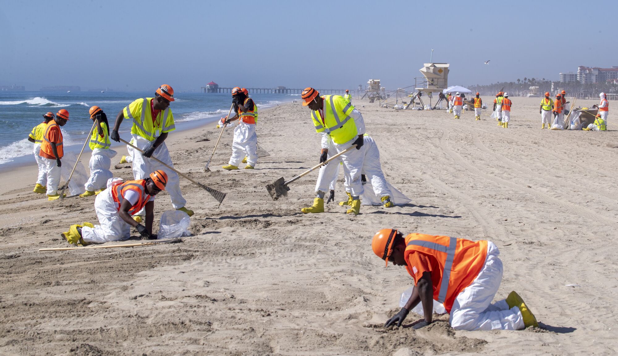 Crew members in yellow and orange vests rake and sift sand on the beach