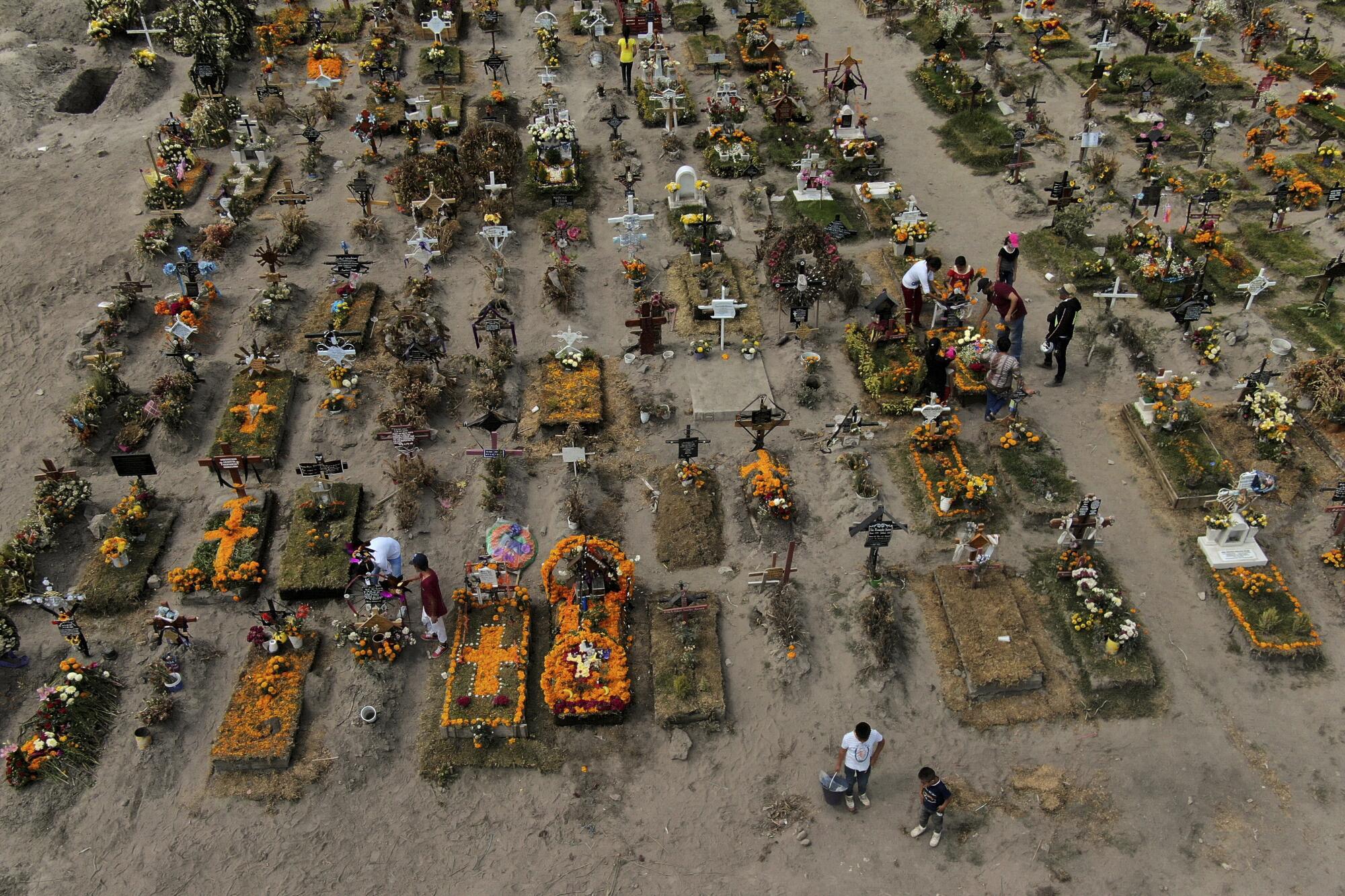 An aerial view of rows of graves adorned with flowers in a dirt graveyard