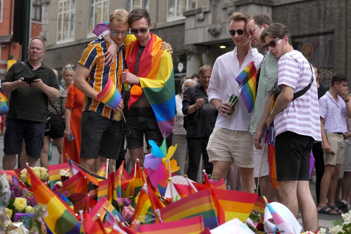 People look on as they lay flowers and hold small Pride flags at the scene of a shooting.