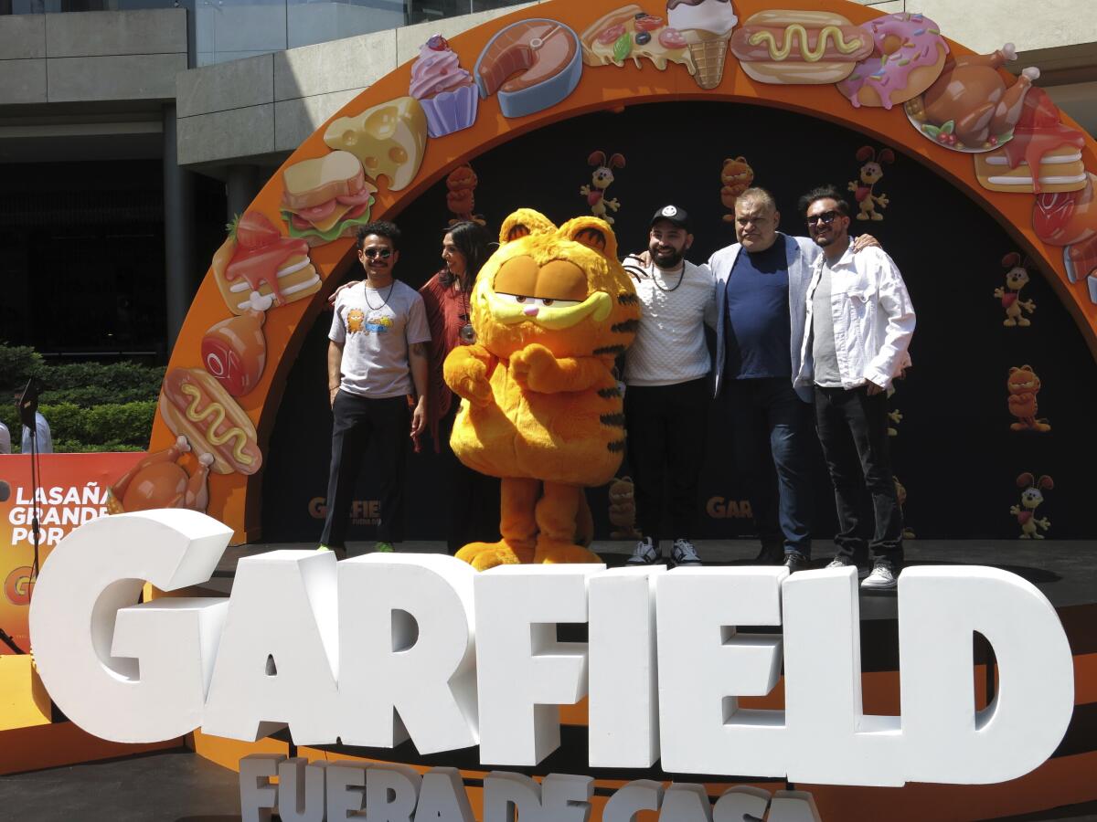Un artista disfrazado como el personaje Garfield, centro, con los actores de doblaje Guillermo 