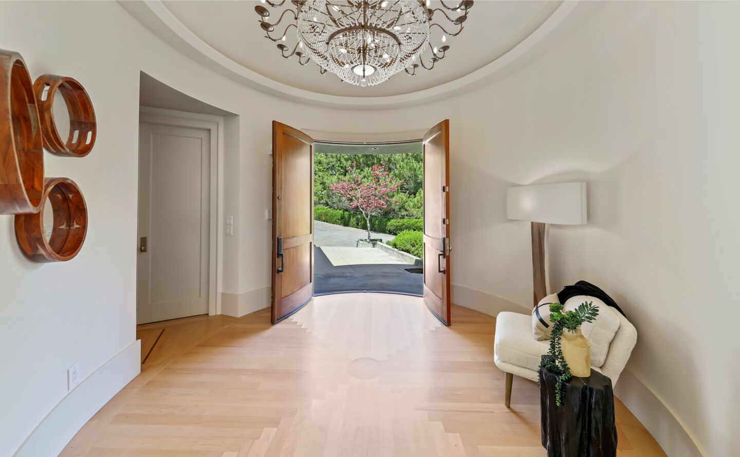 Double wooden doors are open to the front porch in a room with a chandelier and wood floor.