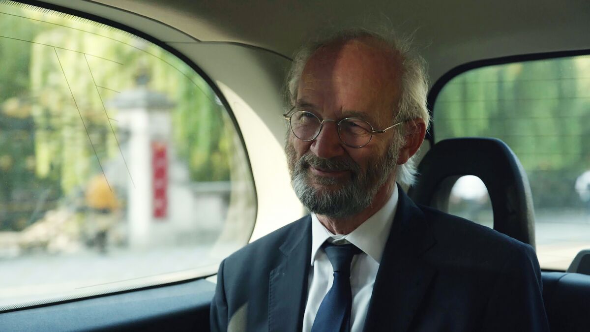 A bearded man in a suit and tie rides in a car in the documentary "Ithaka."