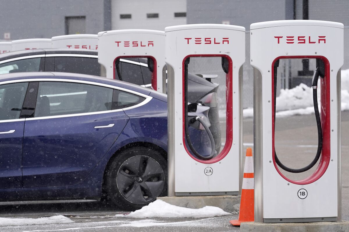 FILE - A Tesla electric vehicle, left, sits in a charging station at a dealership, Thursday, Feb. 18, 2021, in Dedham, Mass. Shares of Tesla tumbled around 4% in premarket trading, Tuesday, Nov. 2, after its CEO and founder Elon Musk tweeted that a deal to sell 100,000 cars to Hertz had not been signed, suggesting it was not final. . (AP Photo/Steven Senne)