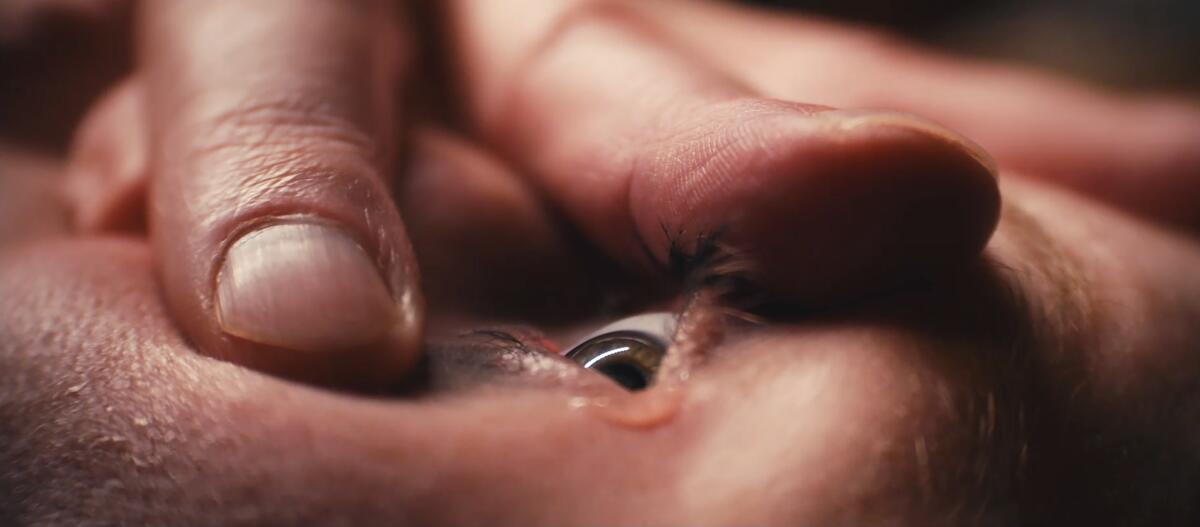 An eyeball is held open by a hand