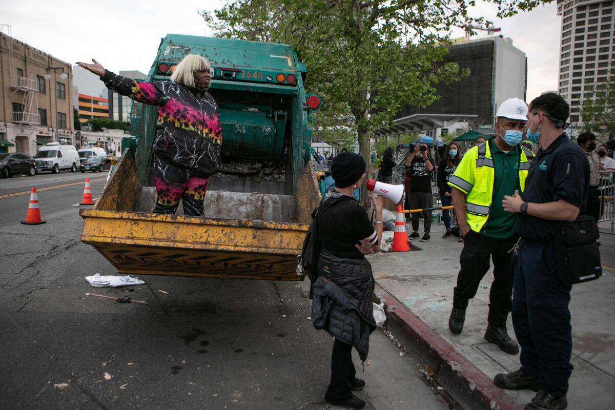 A woman stands inside of a dump truck as the city of Los Angeles clears Toriumi Plaza.