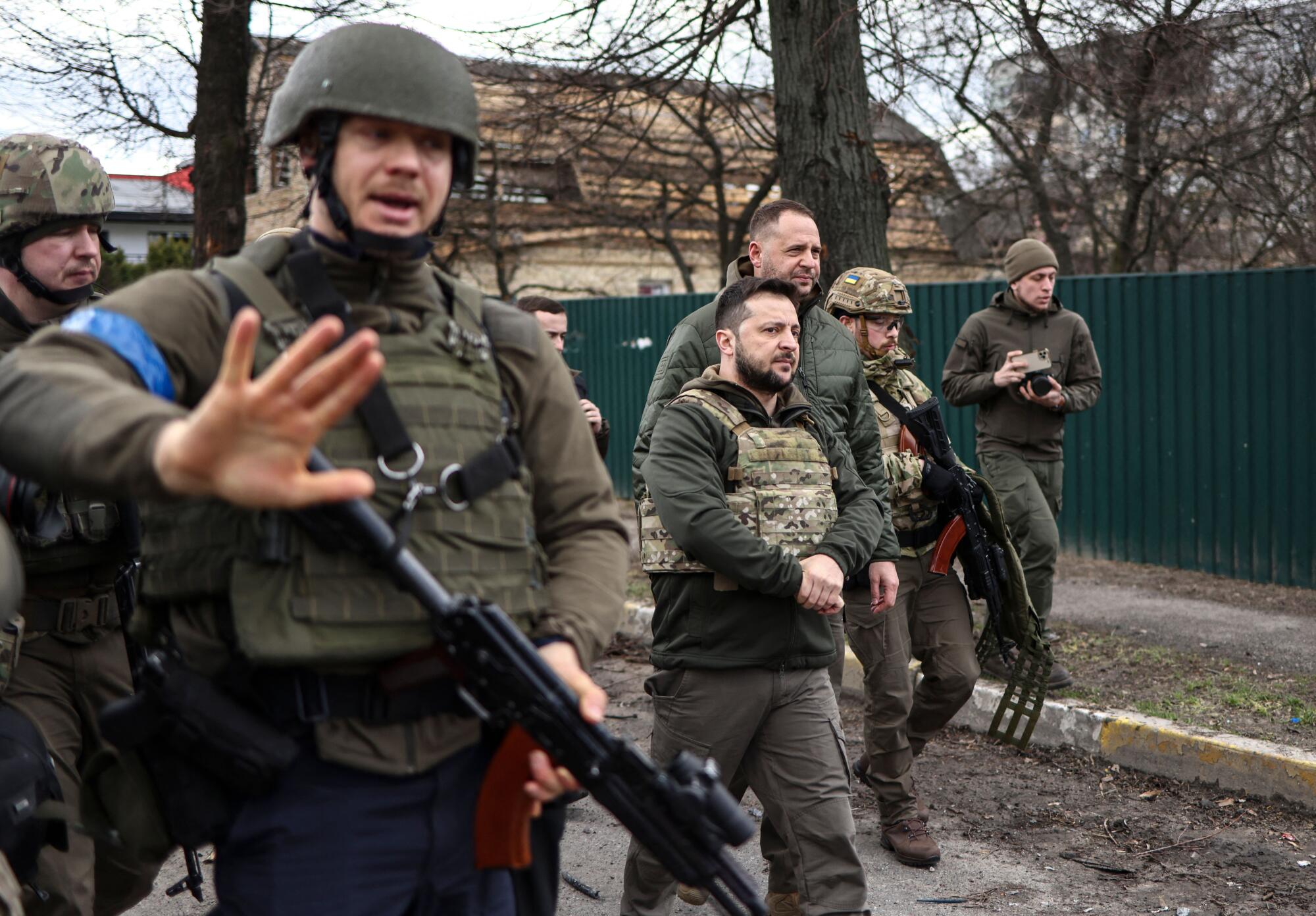 President Volodymyr Zelensky walks in the town of Bucha surrounded by other men with weapons.