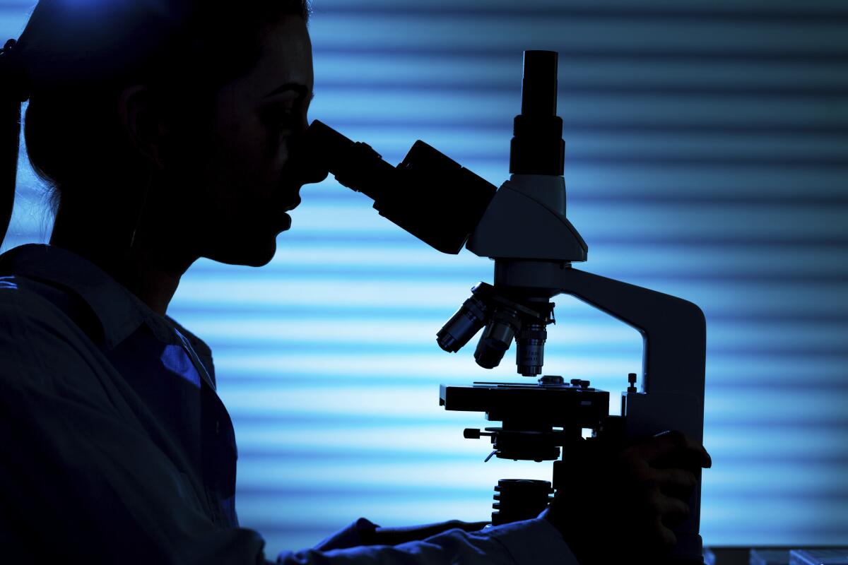 Silhouette of a female scientist using a microscope