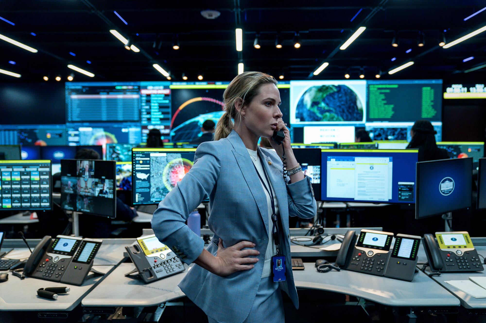 A woman speaks on a phone in front of several monitors.
