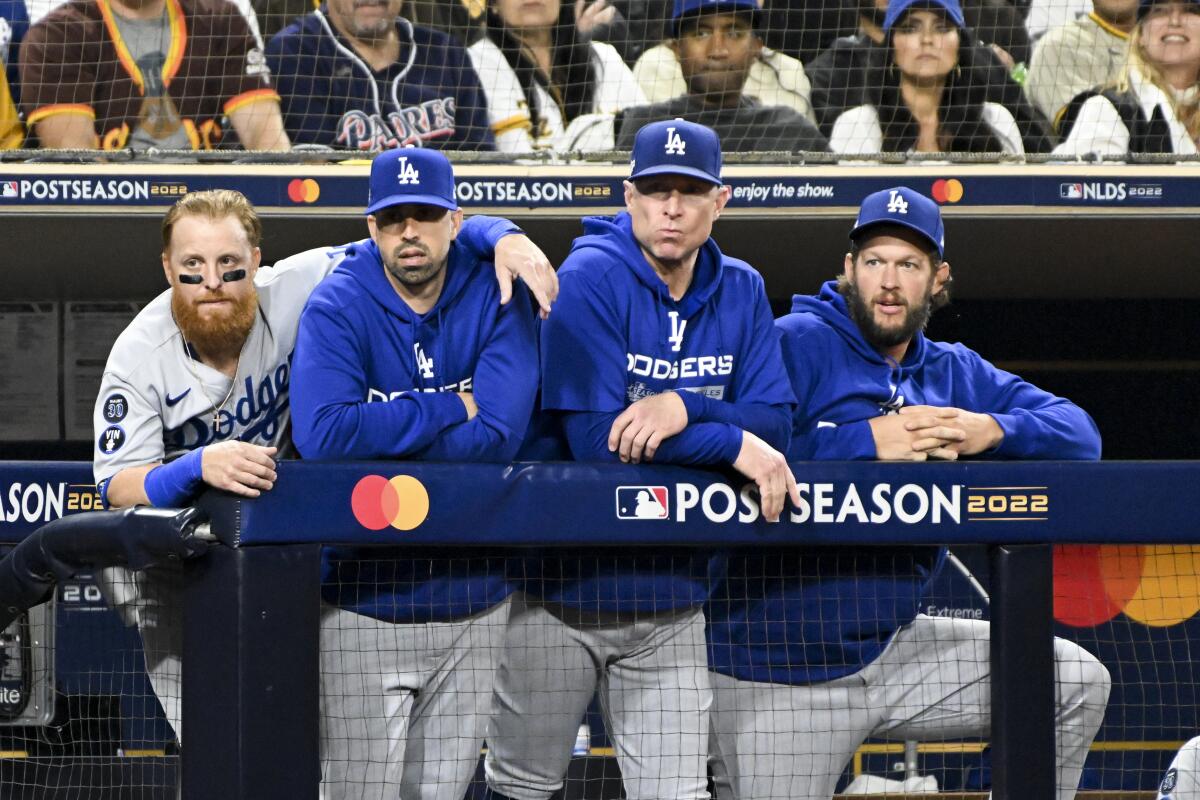 Dodgers slugger Justin Turner wraps his left arm around the shoulders of a teammate while standing along the dugout railing.
