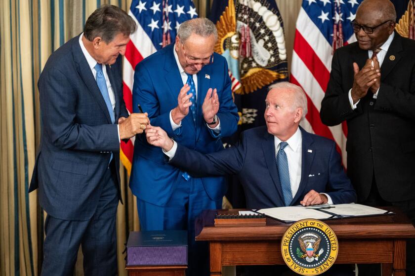 WASHINGTON, DC - AUGUST 16: President Joe Biden, center, hands the pen used to sign H.R. 5376, the Inflation Reduction Act of 2022 into law, to Sen. Joe Manchin (D-WV) in the State Dining Room of the White House on Tuesday, Aug. 16, 2022 in Washington, DC. The 737 billion dollar bill focuses on climate change, lowering health care costs and creating clean energy jobs. (Kent Nishimura / Los Angeles Times)