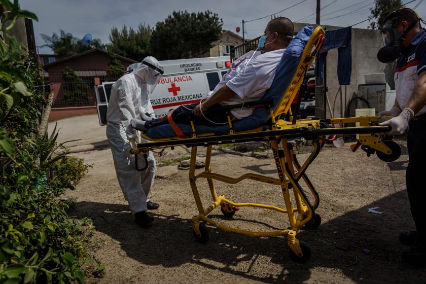 TIJUANA, BAJA CALIFORNIA -- WEDNESDAY, APRIL 29, 2020: Wearing protective suits and equipment, Red Cross paramedics push Eduardo Dionisio Molina, 41, who has symptoms related to COVID-19, out on a stretcher towards an ambulance for transport to a nearby hospital from his home in the Pobladoejido Matamoros neighborhood of Tijuana, Mexico, on April 29, 2020. (Marcus Yam / Los Angeles Times)