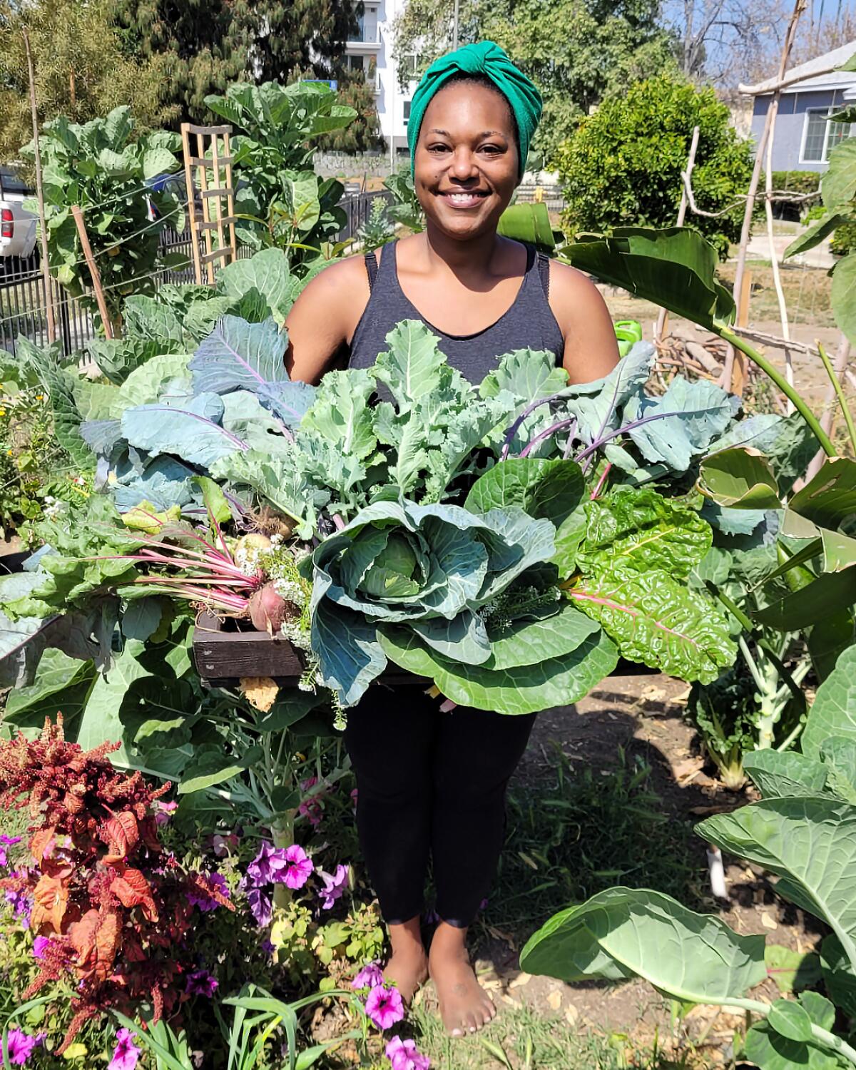 A woman in a garden holds a giant bunch of greens 