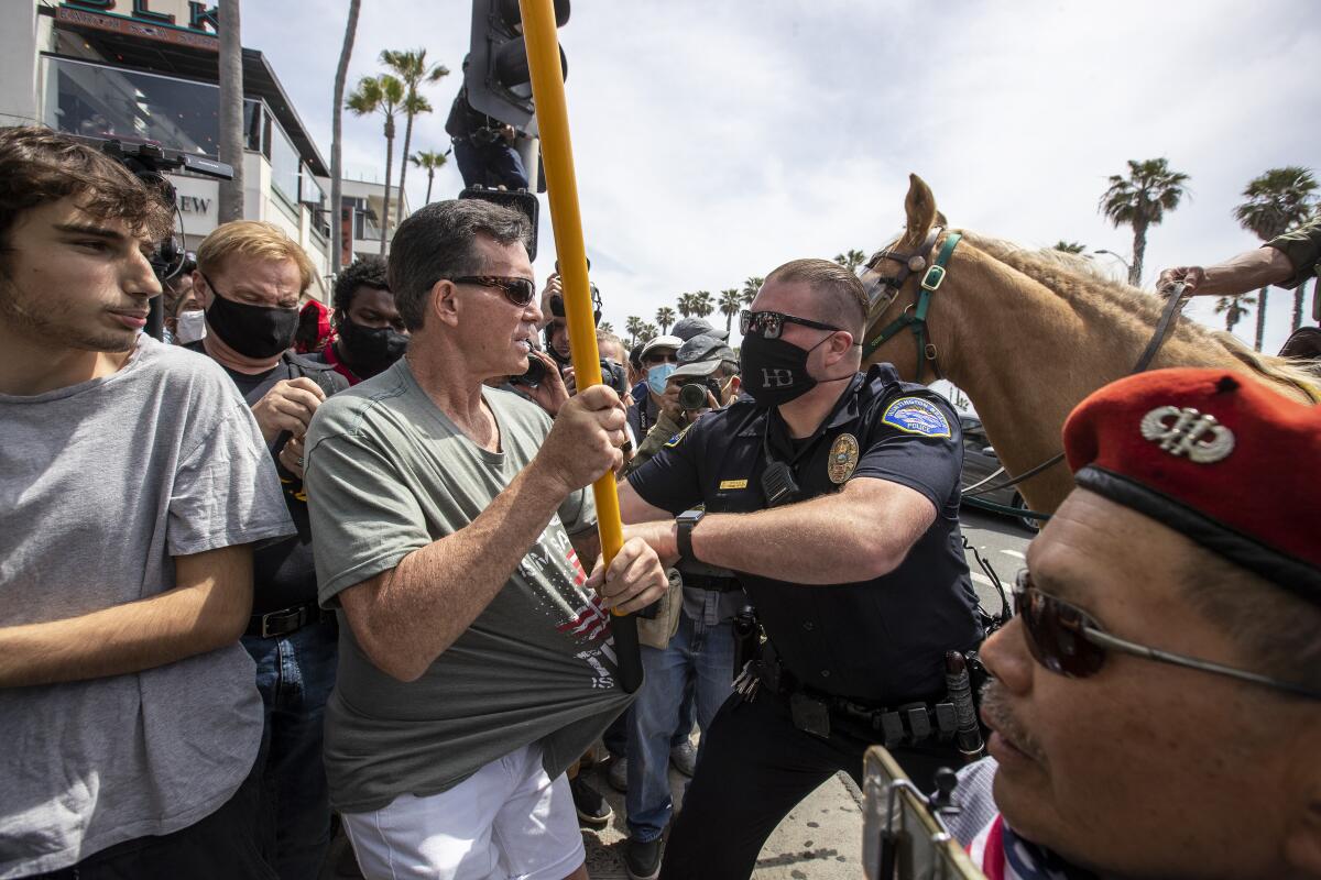 A Huntington Beach police officer arrests a man carrying a Gadsden flag at Sunday’s dual rallies