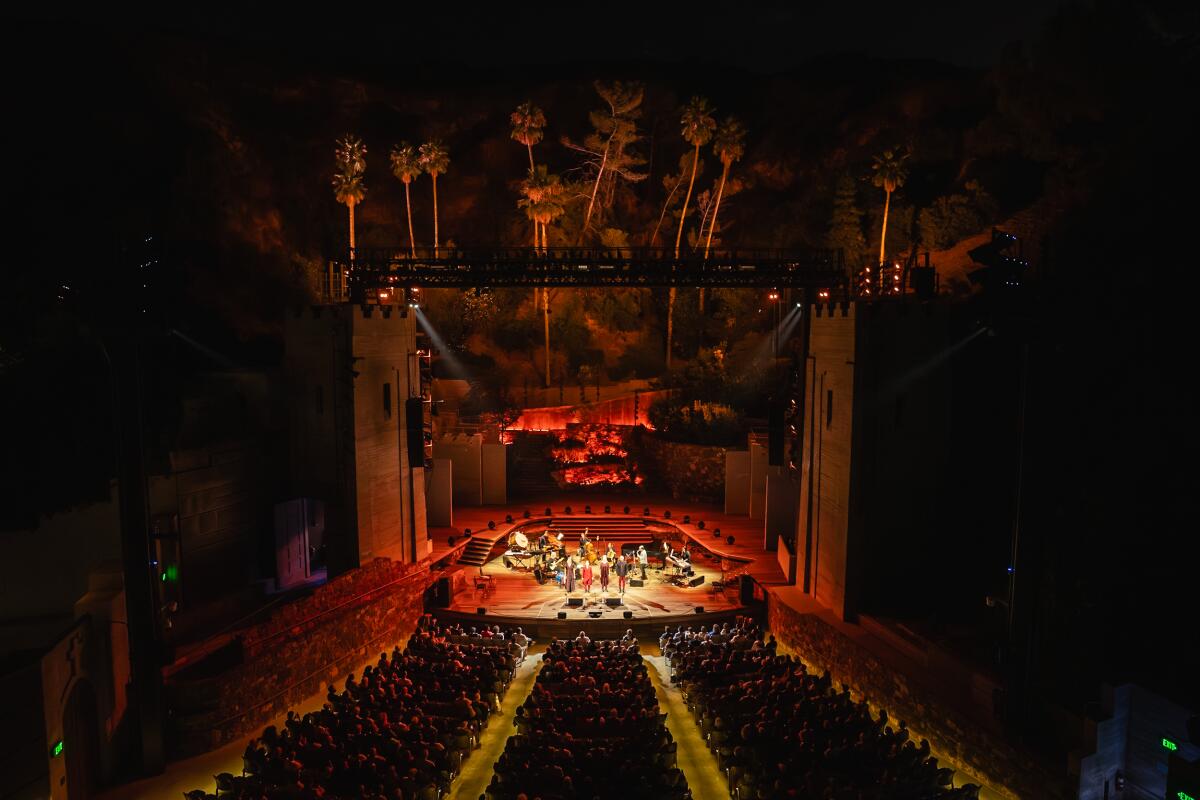 An outdoor stage dramatically lit in the colors of flame is seen from a distance at night.