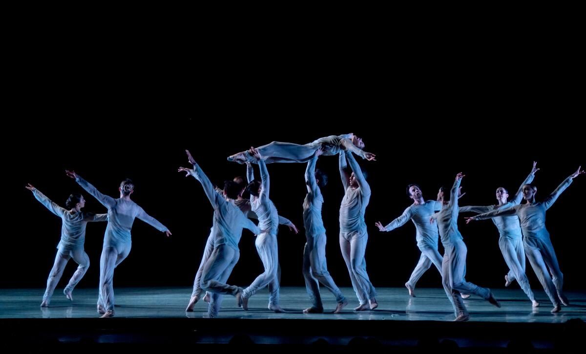 Ballet dancers run in a circle on stage as one is carried in the air. 