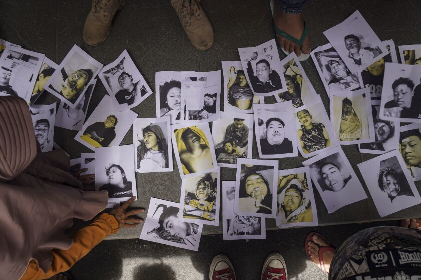 Gente que busca por sus familiares observa fotos de las víctimas de la estampida en un estadio de fútbol en Malang, Indonesia, el domingo 2 de octubre de 2022. (AP Foto/Dicky Bisinglasi)