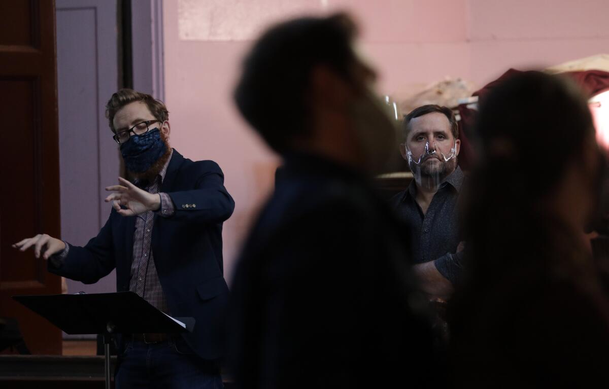 A conductor in a mask leads musicians rehearsing an opera