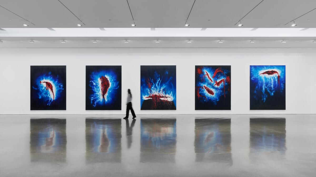 five large paintings on a wall, with a person walking by