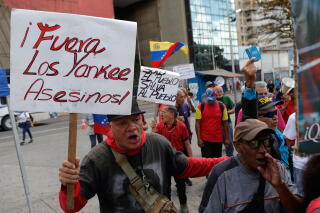 A man holds a sign with a message that reads in Spanish; "Yankee out, murderers" during a protest