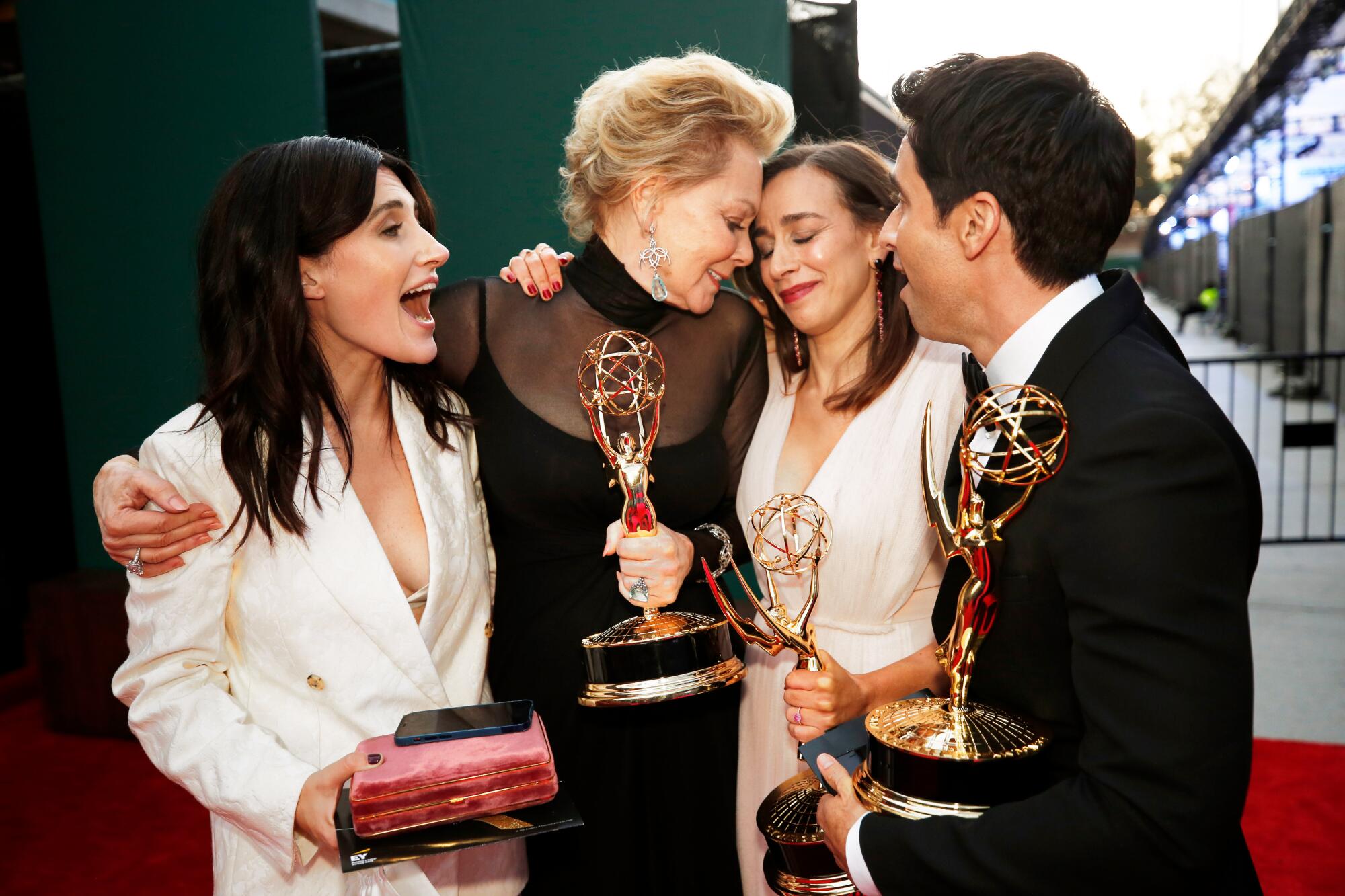 Three women and a man, right, stand shoulder to shoulder. Three of them are holding statuettes