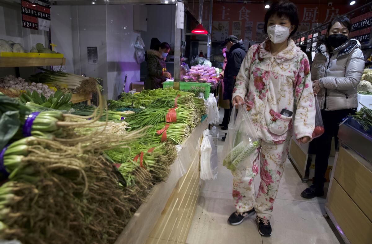 Una mujer que porta una mascarilla y va vestida en piyama adquiere verduras en una tienda en Beijing, China, el martes 18 de febrero de 2020. (AP Foto/Ng Han Guan)