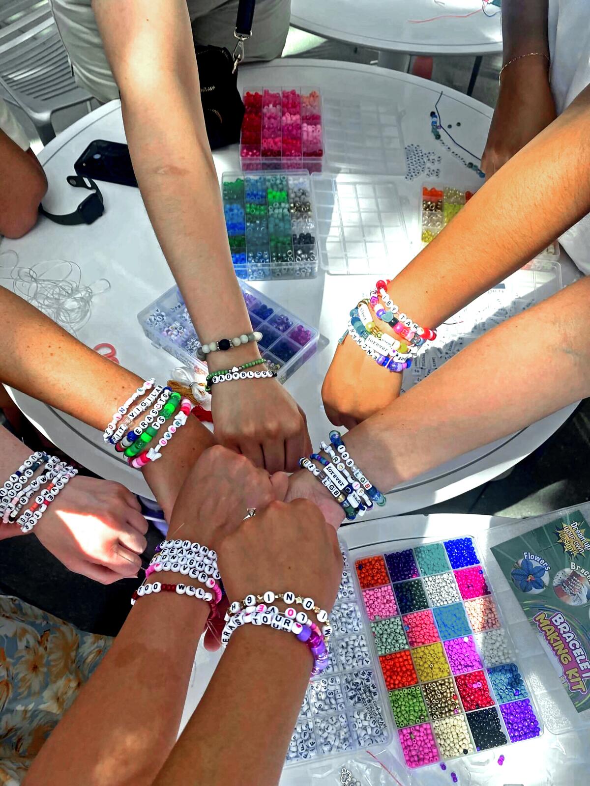 Bracelet makers' hands reach for materials on a table