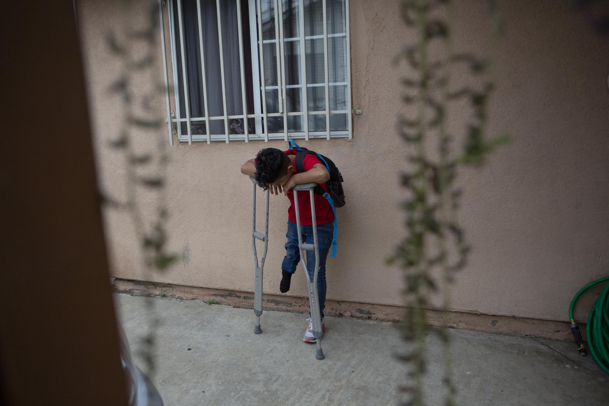 Efrain waits outside his home with crutches