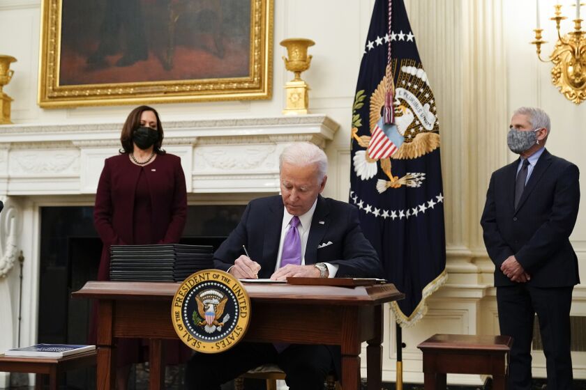 President Joe Biden signs executive orders after speaking about the coronavirus, accompanied by Vice President Kamala Harris, left, and Dr. Anthony Fauci, director of the National Institute of Allergy and Infectious Diseases, right, in the State Dinning Room of the White House, Thursday, Jan. 21, 2021, in Washington. (AP Photo/Alex Brandon)