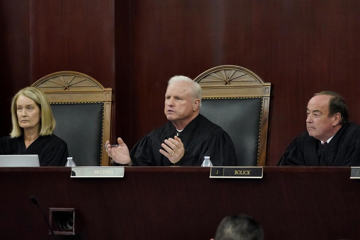 A woman and two men, all wearing black judicial robes, sitting at a table at the head of a hearing room