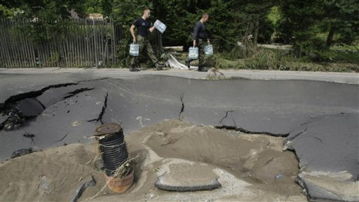 Fire fighters carry water past a destroyed road after a flash floods hit the town of Bogatynia, Poland, Sunday, Aug. 8, 2010. The flooding has struck an area near the borders of Poland, Germany and the Czech Republic.(AP Photo/Petr David Josek)