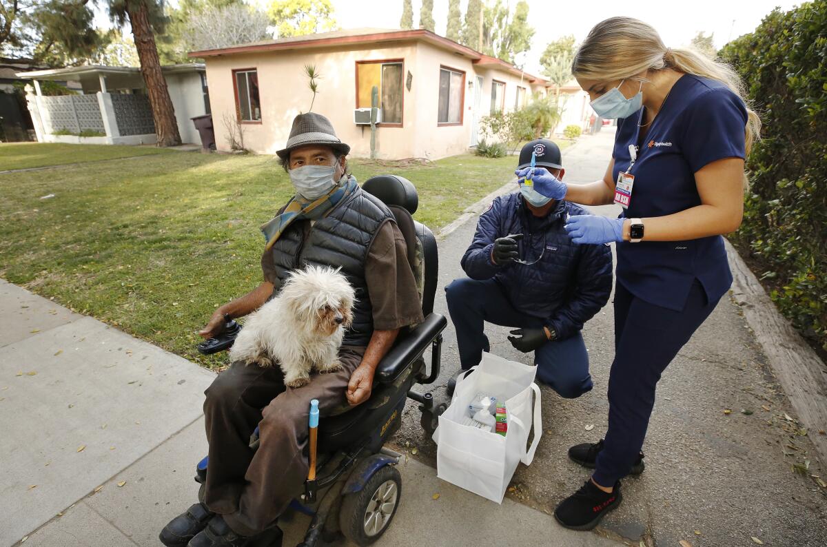A man in a wheelchair with a dog on his lap waits to be vaccinated by a nurse and firefighter 