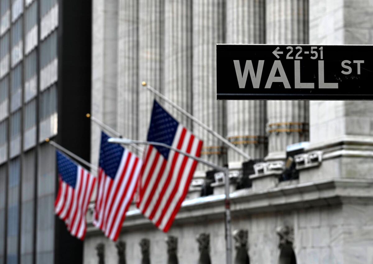 Three flags are to the left of a Wall Street street sign outside the New York Stock Exchange.