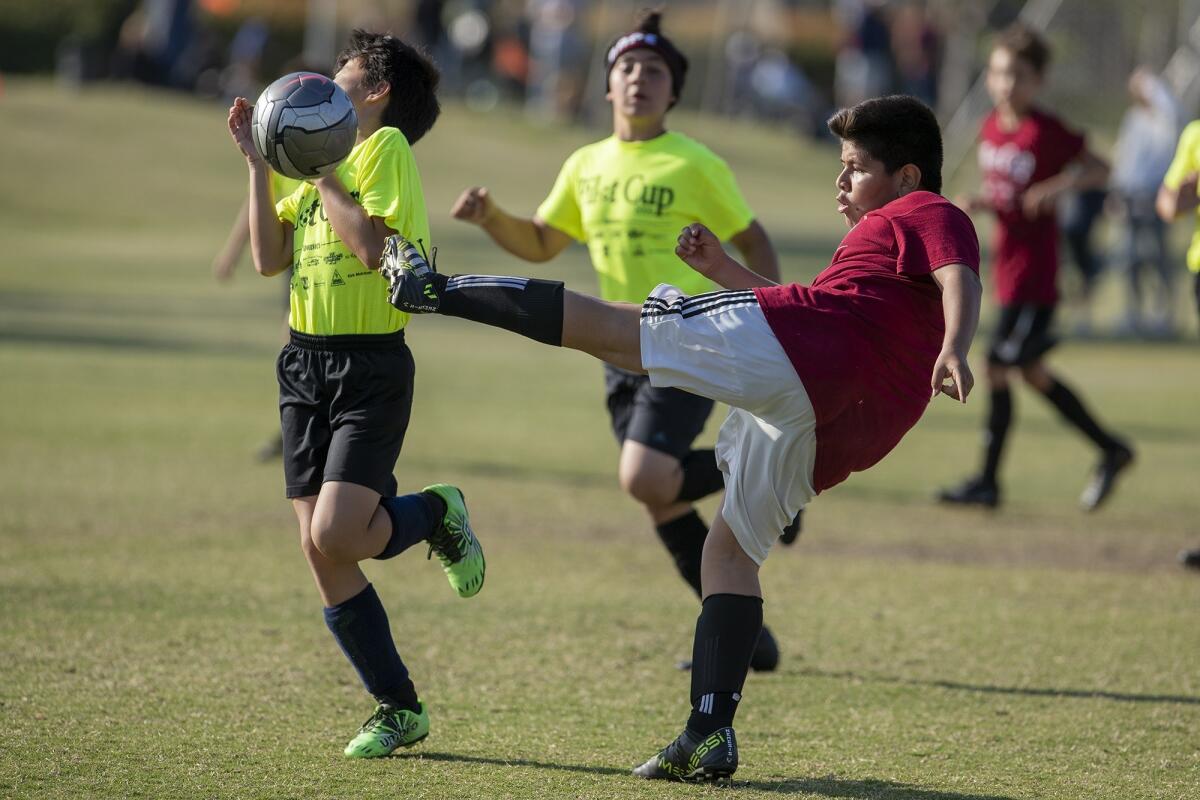 Pomona Elementary's Jorgely Mendez, right, kicks a ball into Newport Coast's Jordan Lum in a boys' fifth- and sixth-grade Silver Division pool-play match at the Daily Pilot Cup at Jack R. Hammett Sports Complex in Costa Mesa on Thursday.