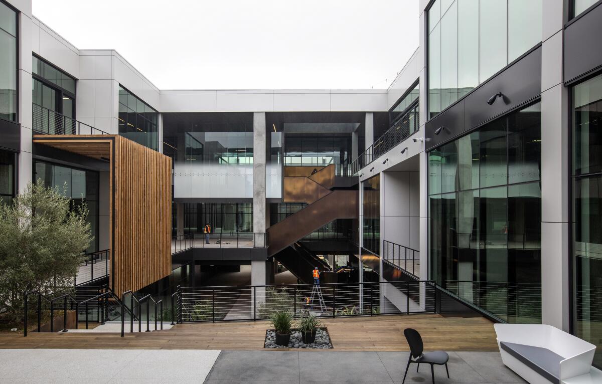 Seating is seen in the courtyard of a multistory office building that has a wood patio and dark glass walls. 