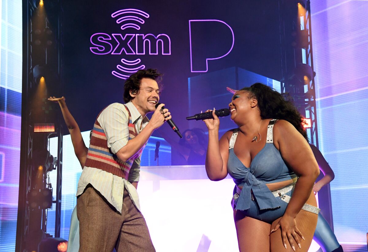 A man and a woman face each other while singing into microphones on a stage.