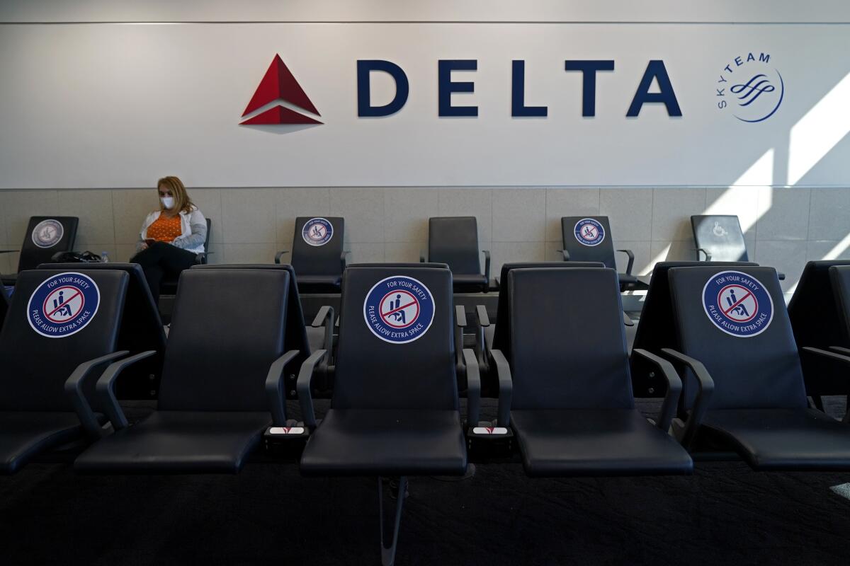 Una pasajera con mascarilla espera en un área de distanciamiento social para un vuelo de Delta Airlines