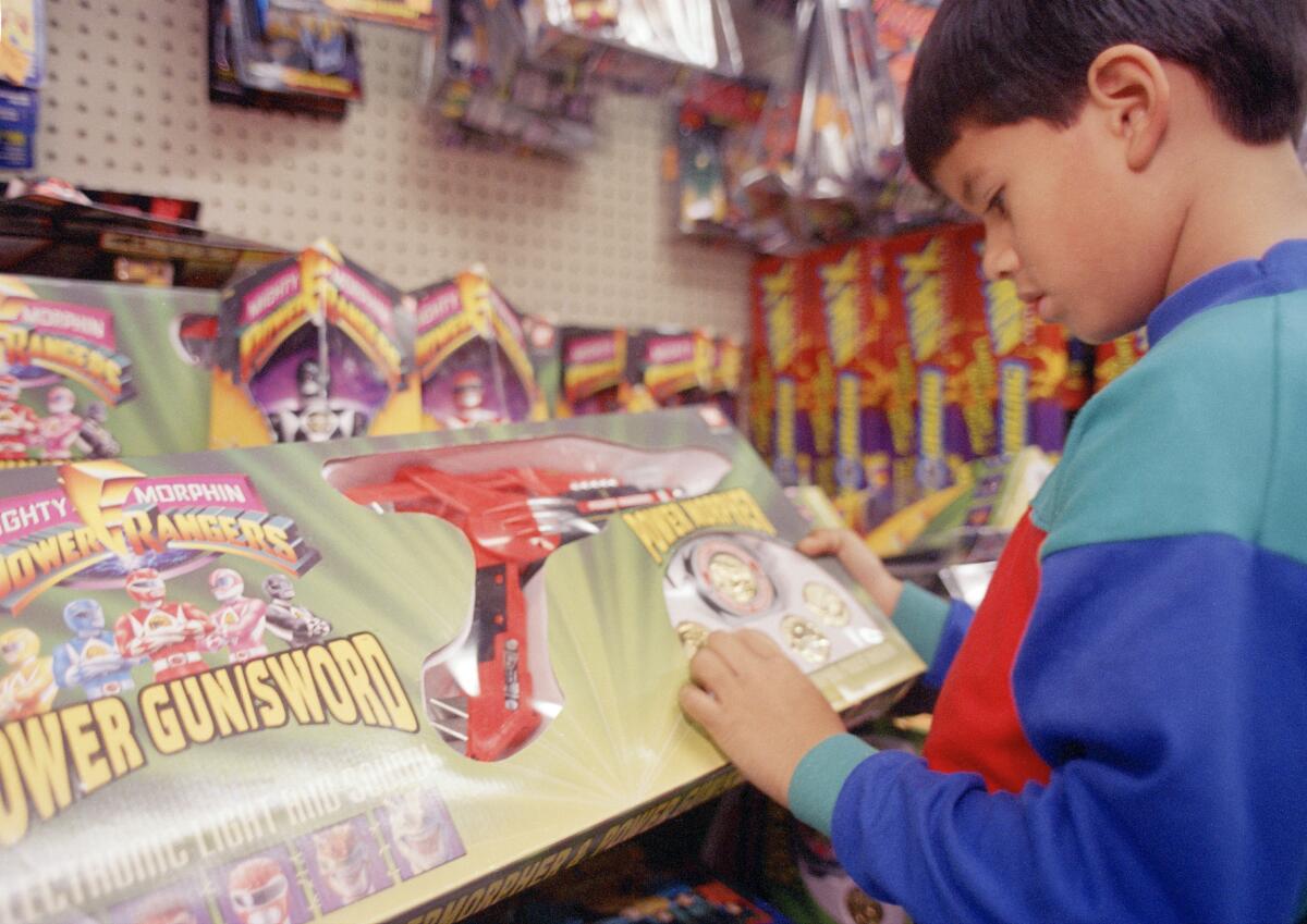 A child looks at a Mighty Morphin Power Rangers power gun/sword at a toy store.