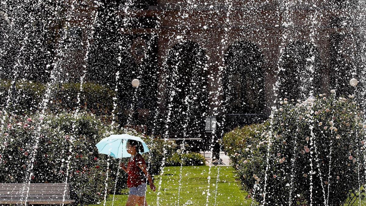 A woman walks past the fountain at Exposition Park, where temperatures reached into the 90s.