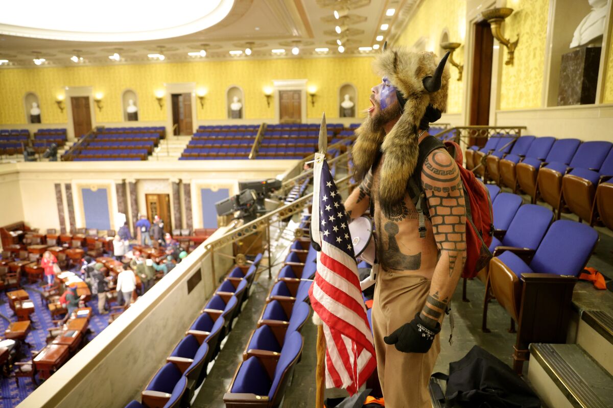 A shirtless man covered in tattoos, wearing a fur Viking hat and carrying an American flag yells inside the Senate chamber.