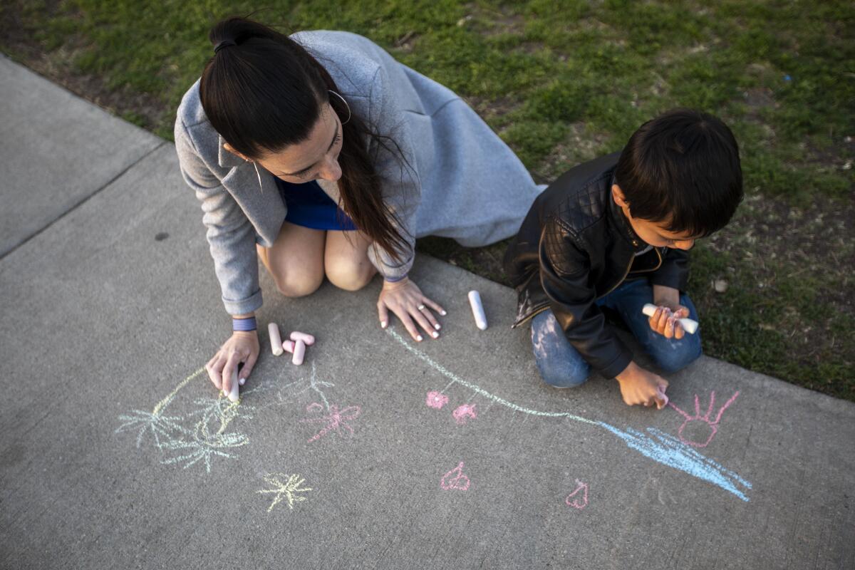 A mother and son draw with chalk on the sidewalk