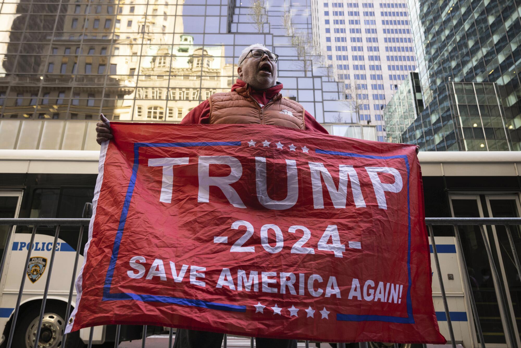 A supporter of former President Donald Trump holds a "Trump 2024 — Save America Again!" flag.