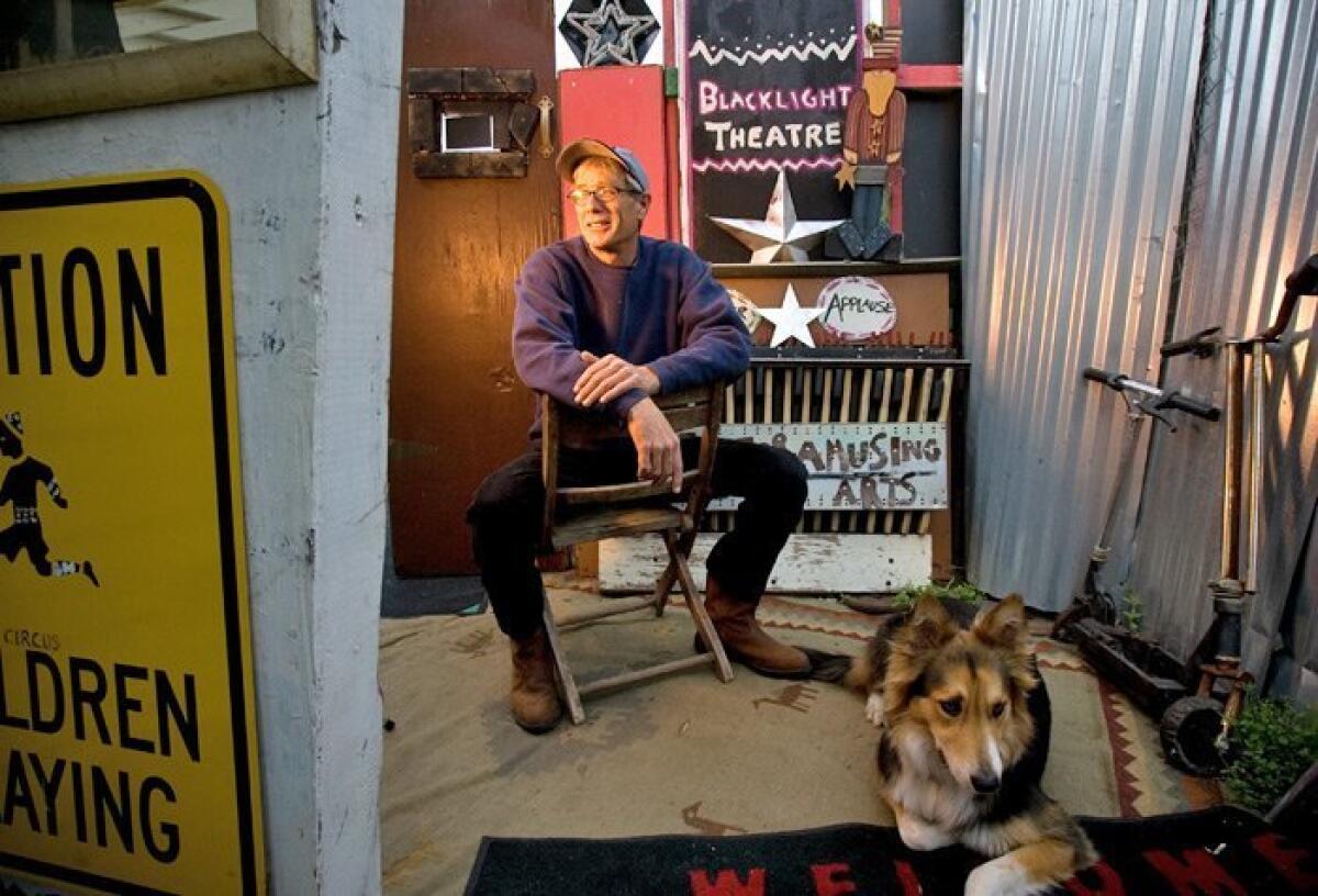 Bruce Cartier, at the entrance of his at-home performance space with his dog, Springer — was staging green-conscious theater before it was chic. His “no-budget circus” productions in Barrio Logan make use of discards and Craigslist freebies. — Earnie Grafton / Union-Tribune