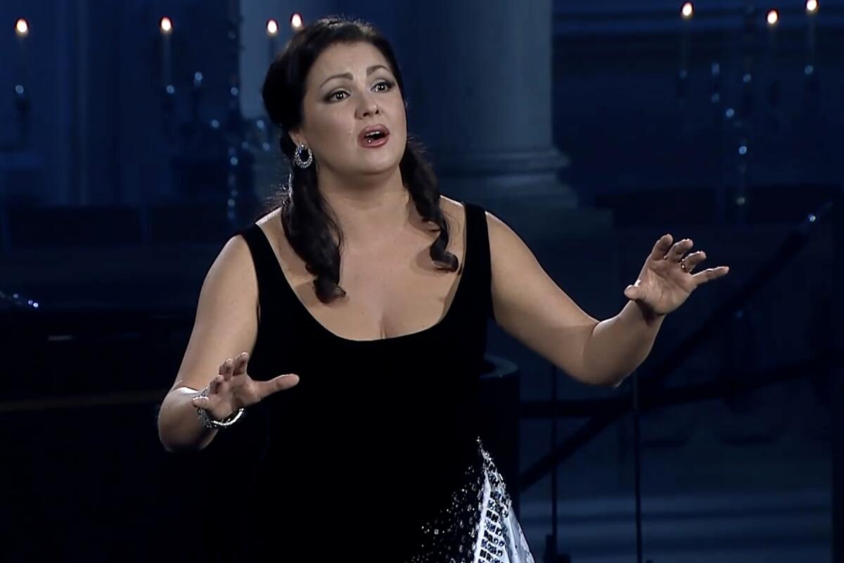 Mezzo-soprano Elena Maximova singing in a black dress, arms raised.