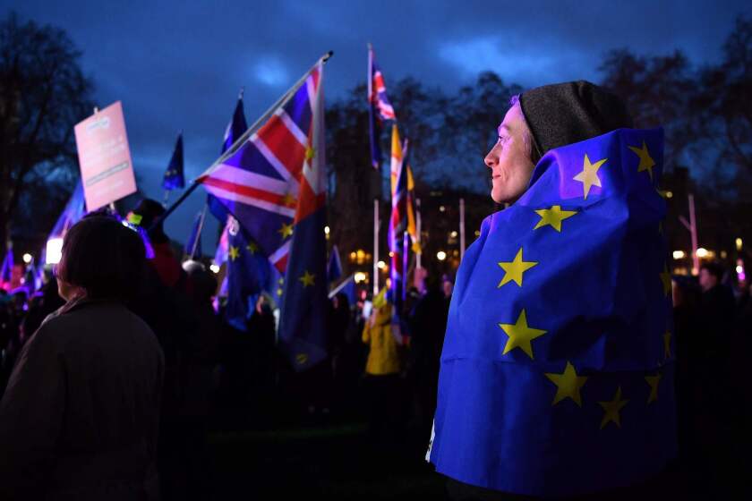 An anti-Brexit activist wrapped in an EU flag stands with other protestors as they demonstrate outside of the Houses of Parliament in central London.