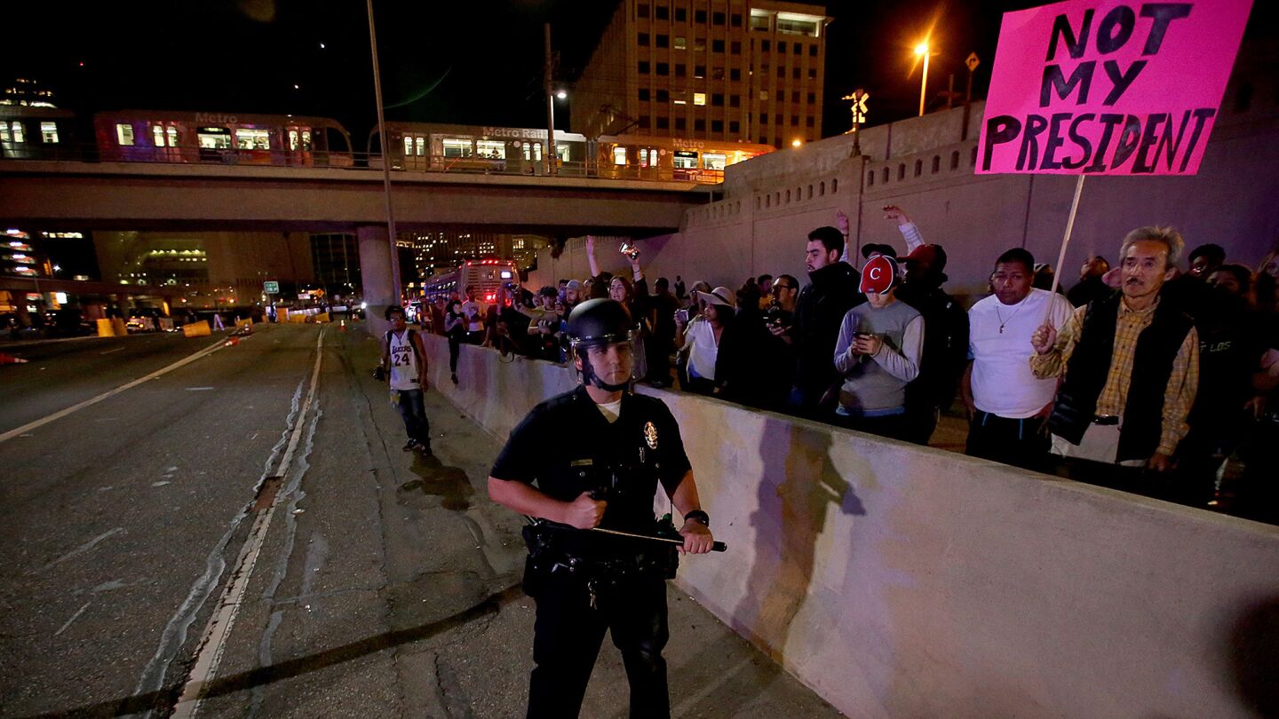 A police officer watches protesters behind a concrete barrier along the 101 Freeway in downtown Los Angeles on Wednesday night.