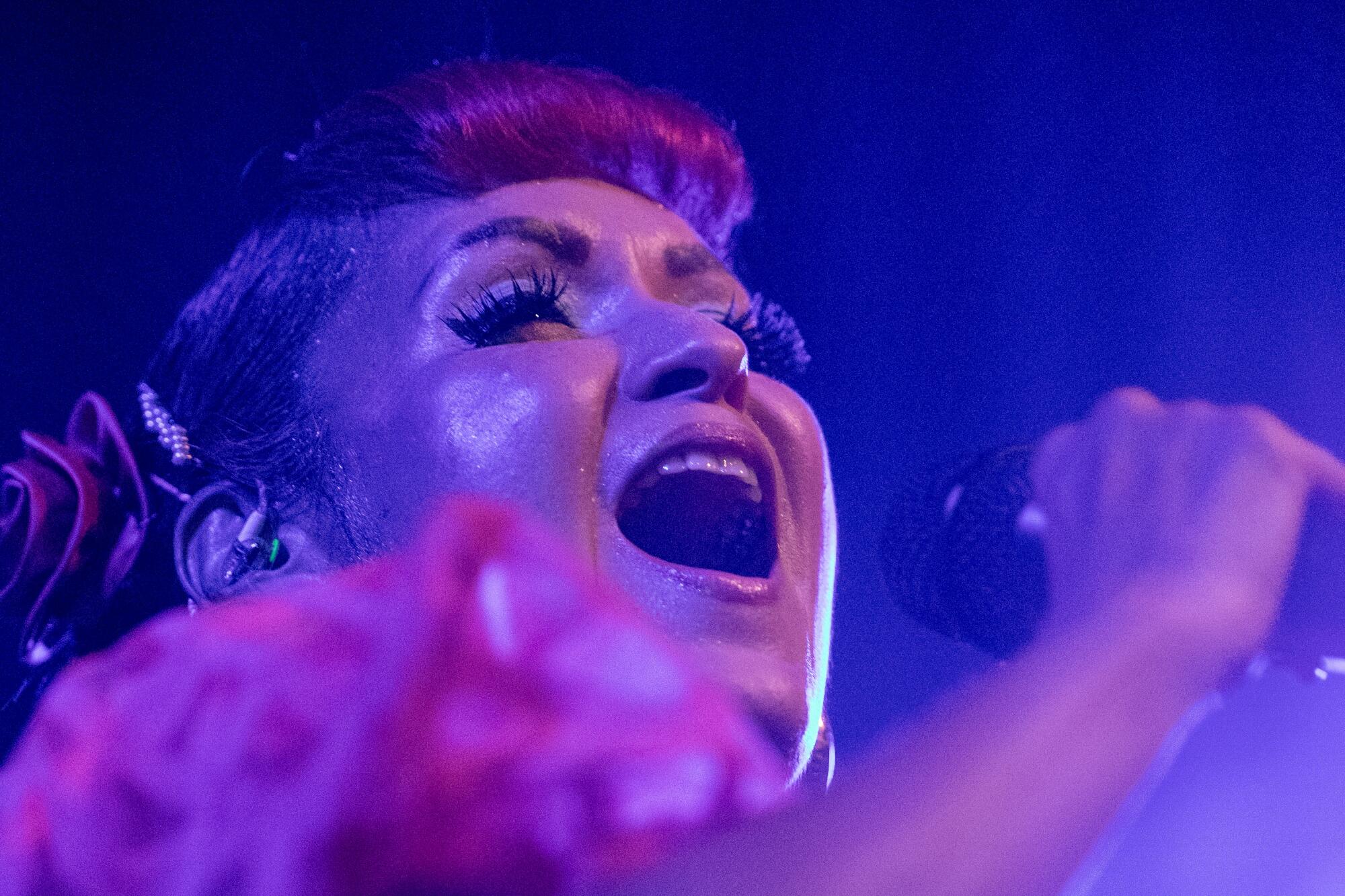 A woman bathed in blue light sings into a microphone.