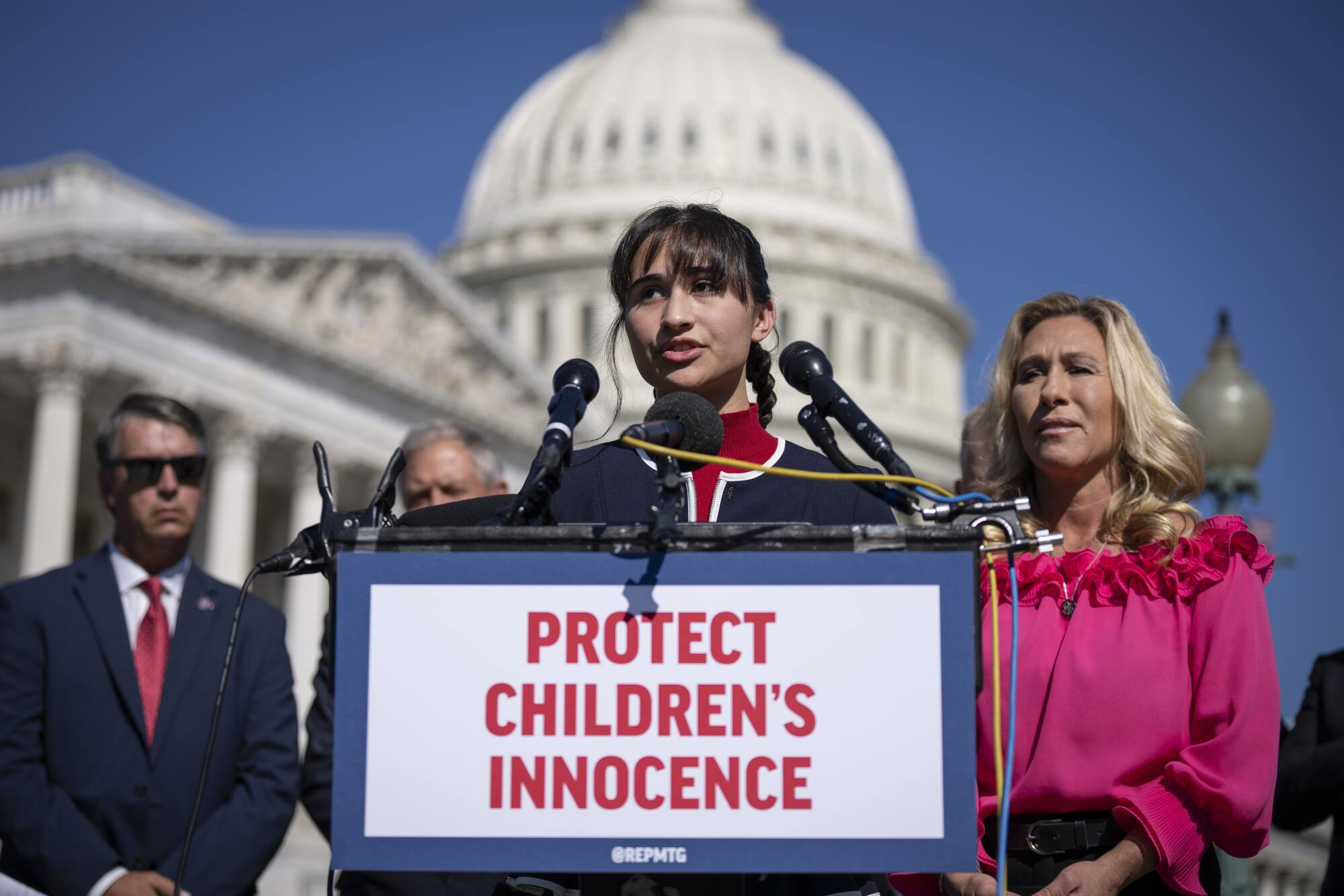 Chloe Cole speaks before a sign that says, "Protect Children's Innocence," outside the U.S. Capitol